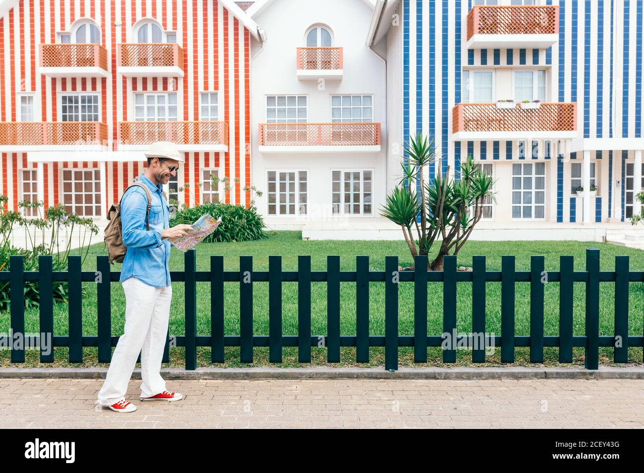 Side view of trendy man with backpack and mat walking against striped colorful houses on Costa Nova do Prado in Portugal Stock Photo