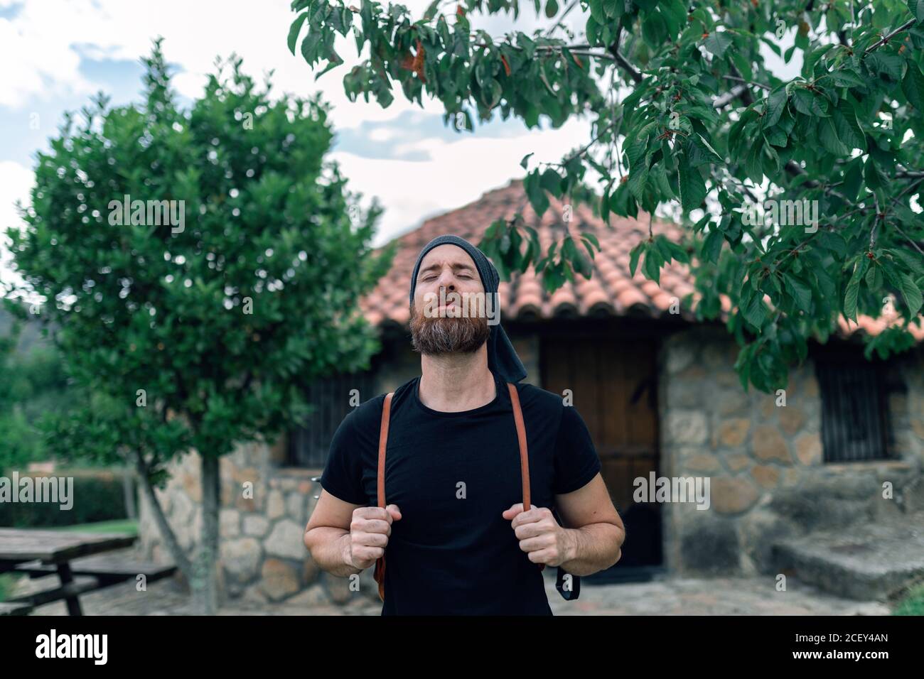 Calm male tourist with backpack standing near stone house in settlement Stock Photo