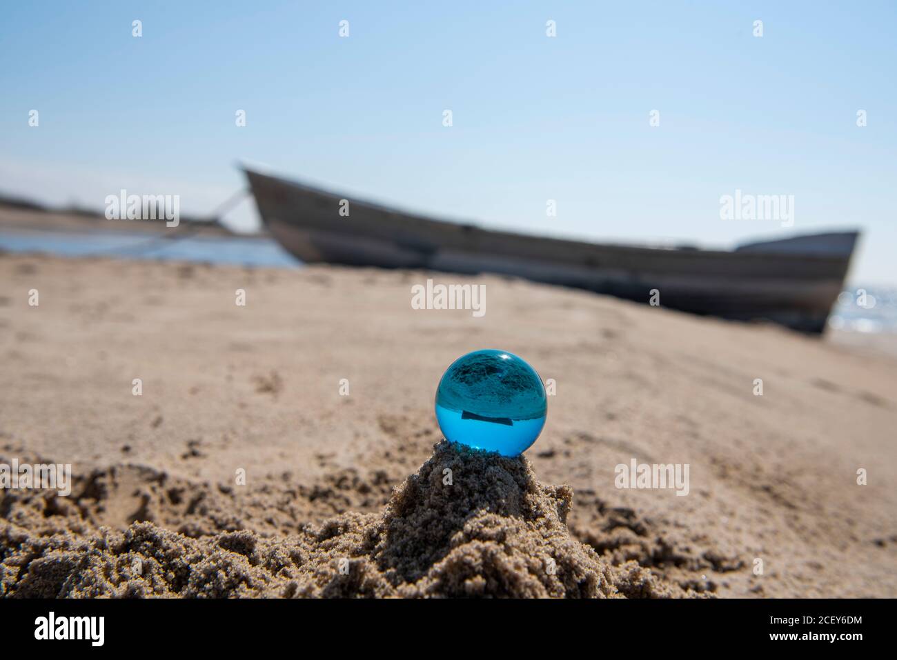 Blue glass ball on sand near the sea. Abstract conceptual photo. Stock Photo