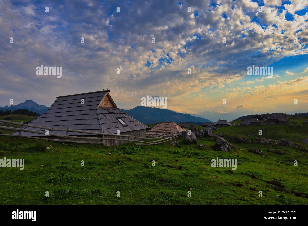 Wooden hut in Velika planina during sunrise. Beautiful photo of agriculture landscape with the view of green grass, wooden cottage and cloudy sky. Stock Photo