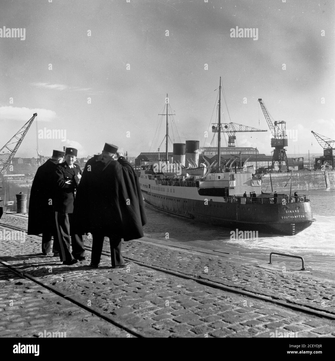 1950s, historical, French gendarmes  on the cobbled quay in Calais, France as a large passenger ferry, Dinard, Southampton, comes into the port. The steam turbine ship, TS Dinard was built in 1924 by William Denny & Bros of Dunbarton for the Southern Railway Company, Southampton, England, UK for the route Southampton - St Malo During WW2 she served at both Dunkirk and Normandy. Following the war, she was rebuilt as a car and passenger ferry and operated between Dover and Boulogne. At this time cars were still crane-loaded onto ships. She remained in service until 1958. Stock Photo