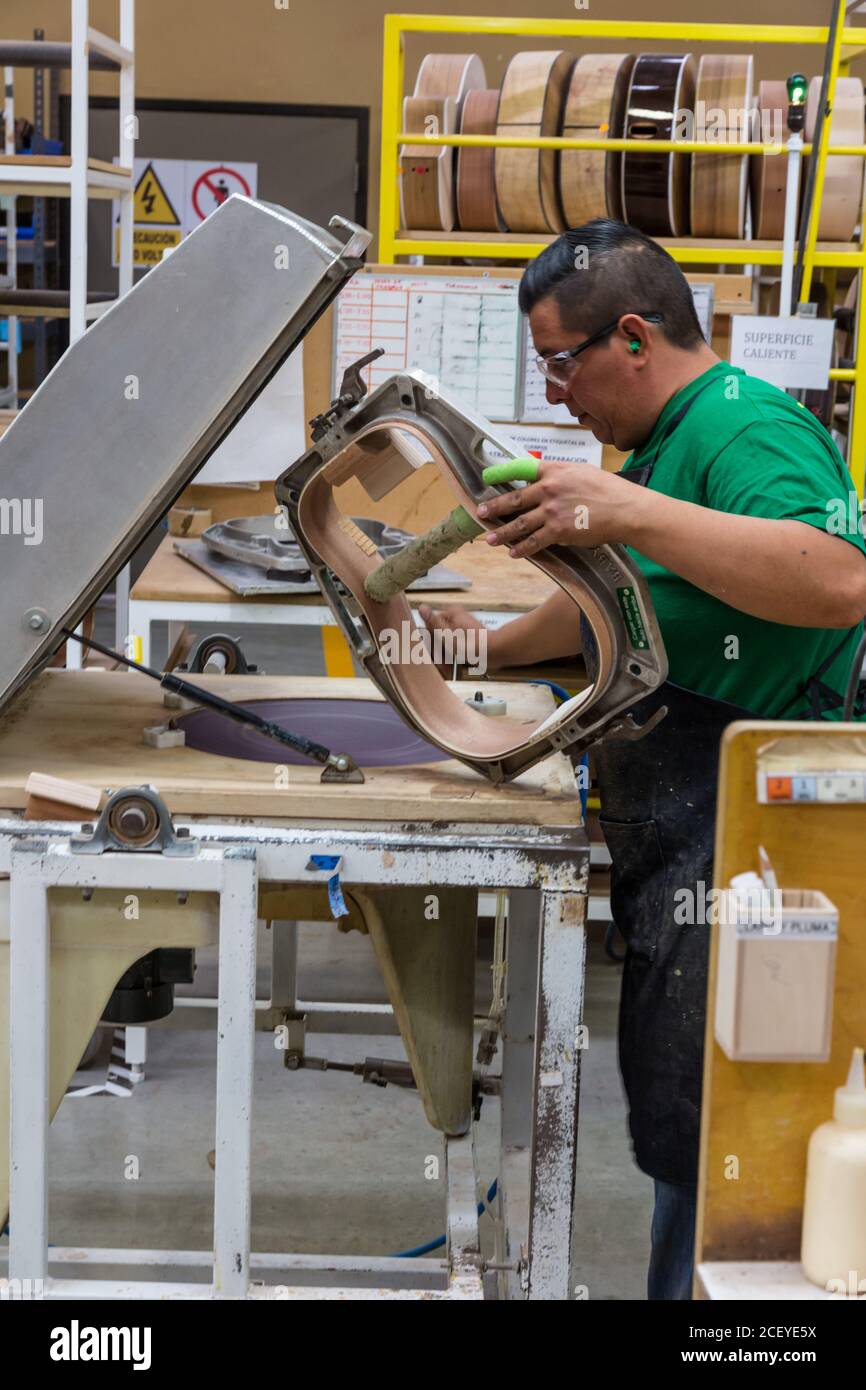 Worker building and assembling guitars at the Taylor Guitar factory in Tecate, Mexico.  This worker is gluing the halves of the guitar body together. Stock Photo