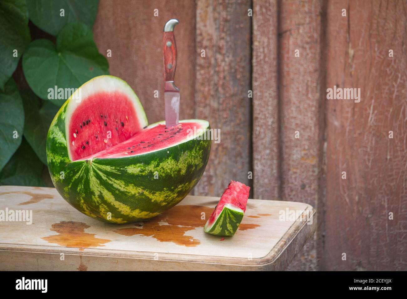 Fresh red watermelon on wooden cutting board near old door to village house, picnic concept, selective focus Stock Photo