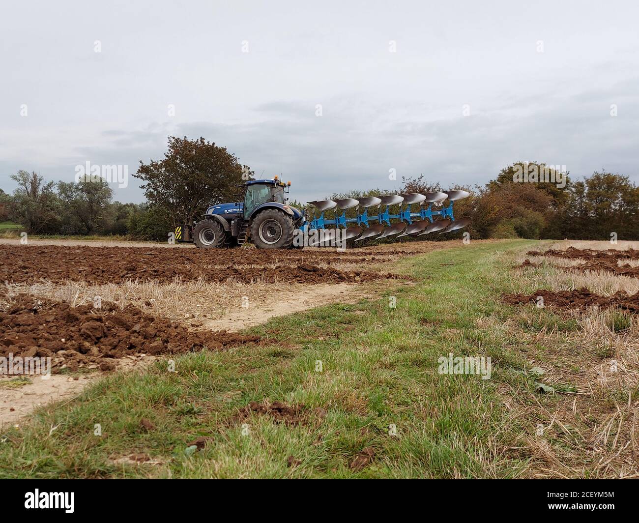 New Holland Tractor Ploughing Arable Farm Land, cloudy sky Stock Photo