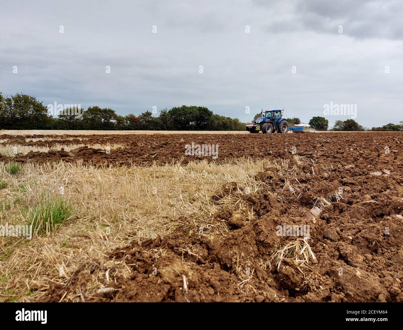 New Holland Tractor Ploughing Arable Farm Land, cloudy sky Stock Photo