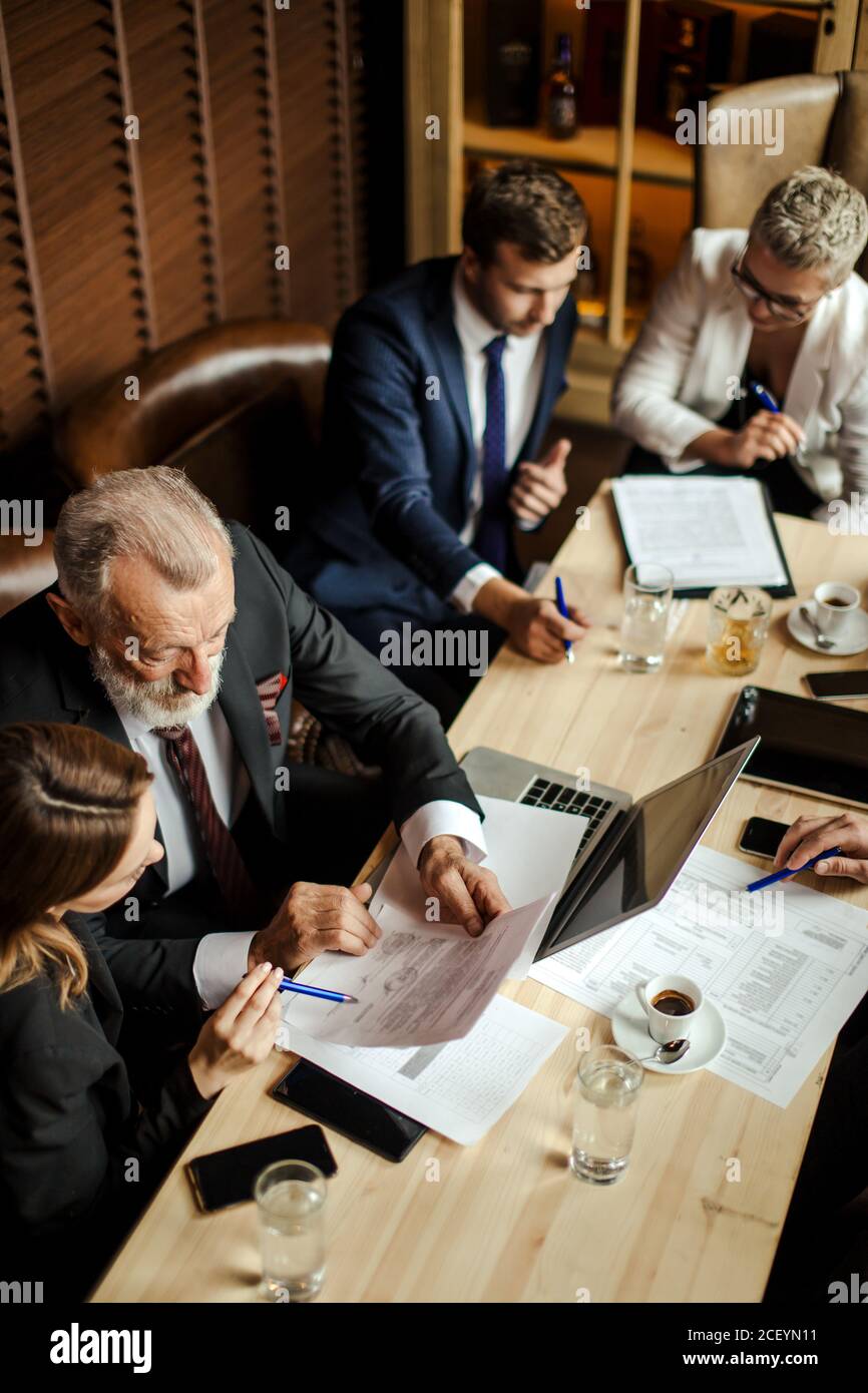 Quick witted professionals solving business problems at general meeting. Broad minded gray haired man reading a contract with his young brunette femal Stock Photo