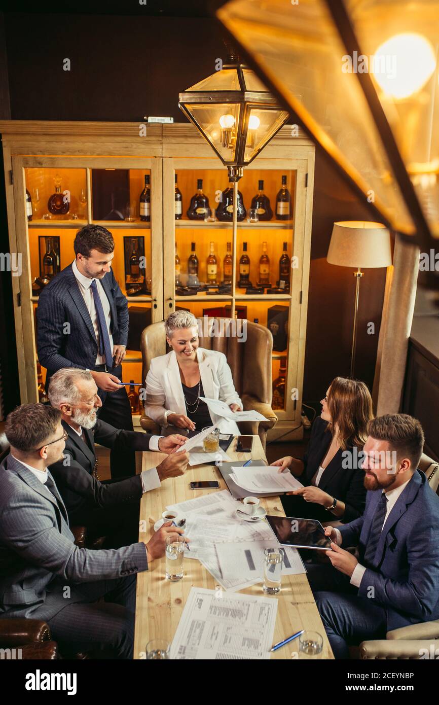 relaxed atmosphere at conferens, business partners smiling, making jokes in office. Papers, sellphones, coffe cus, glasses of wates, laptop, documents Stock Photo