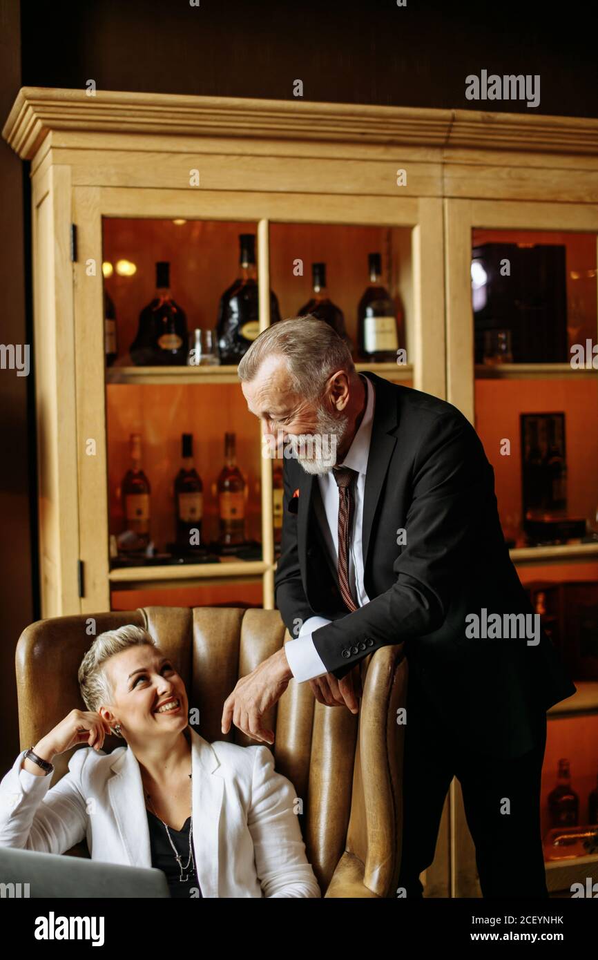 Broad minded businessman with thick beard kindly talking to young female partner in dimly lit cabinet not paying attention to camera Stock Photo
