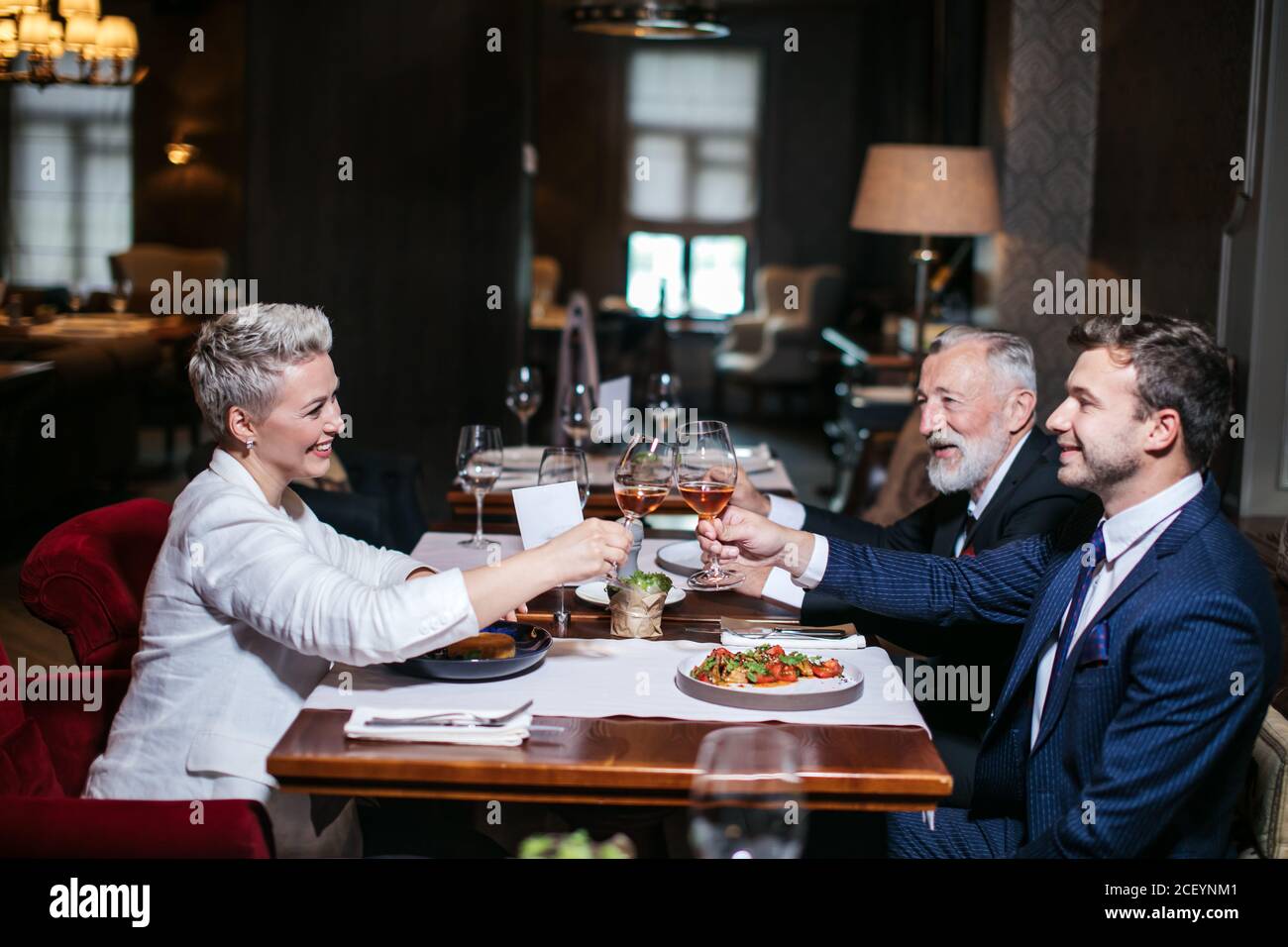 Happy business partners cheerfully raising hands with glasses of wine, gladly congratulate each other with successful deal, posing in luxury restauran Stock Photo