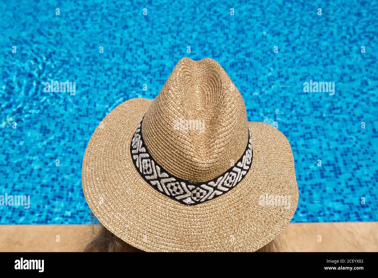 woman in straw hat sunbathing sitting on the edge of swimming poo Stock Photo