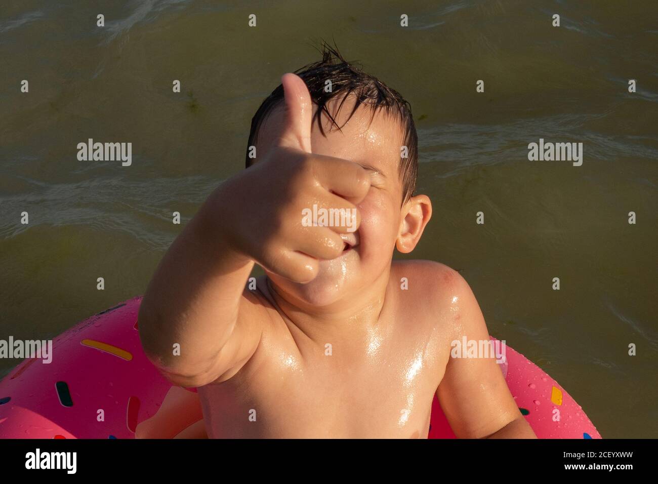 A 5 year old boy swims in the sea, rejoices and has fun in an inflatable ring in the shape of a donut. Stock Photo