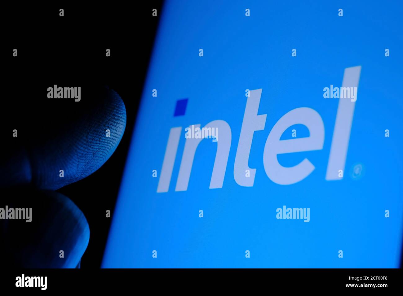 New Intel logo seen on the screen and blurred fingertip touching it in a dark. Intel presented its rebranded logotype o Stock Photo