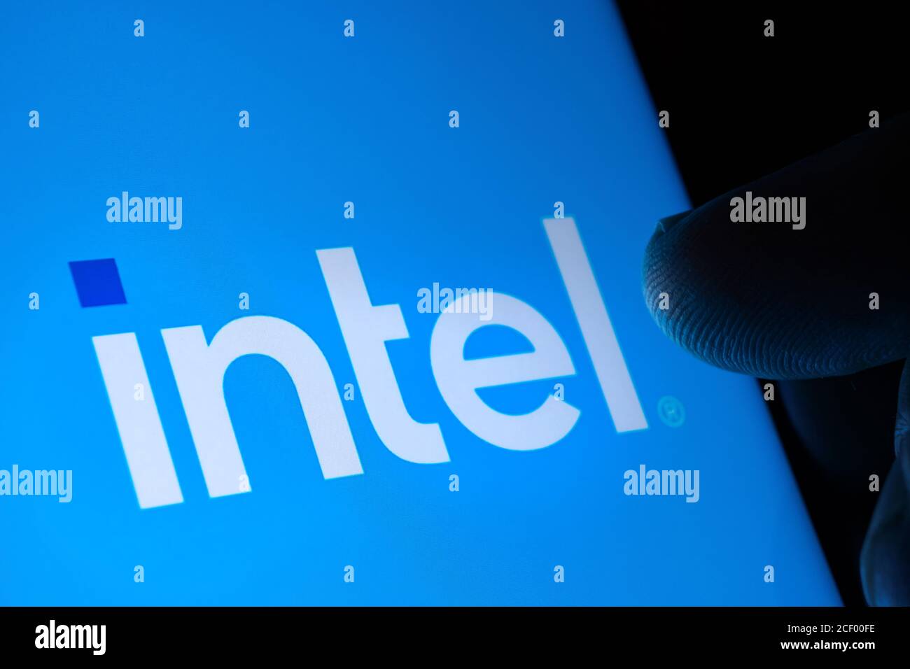 New Intel logo seen on the screen and blurred fingertip touching it in a dark. Intel rebranded its logotype. Selective Stock Photo