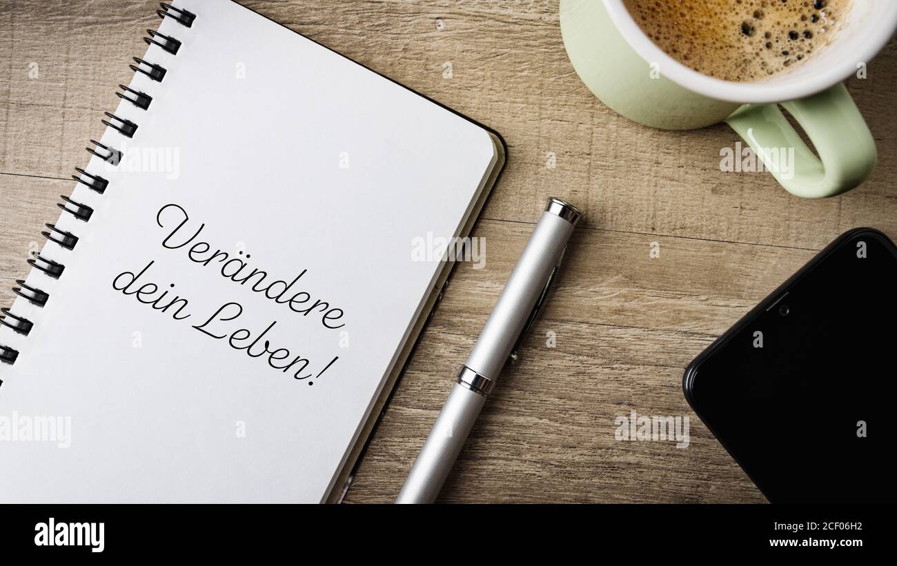 Flat lay. Work area with notepad, pen, cell phone and a cup of coffee. German Text. Translation: Change your life! Stock Photo