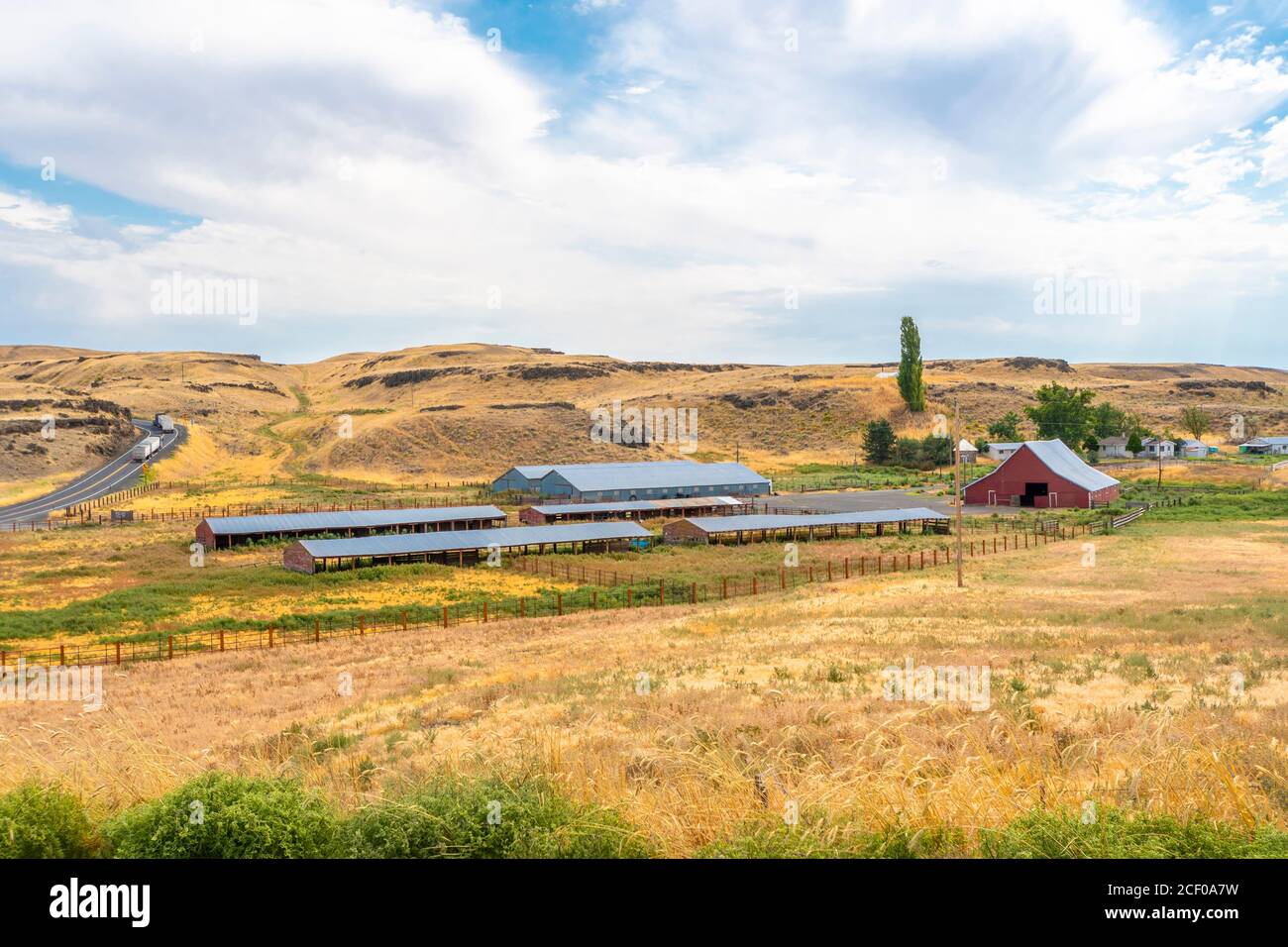 Two trucks drive up a sloping highway next to a large agricultural farm
