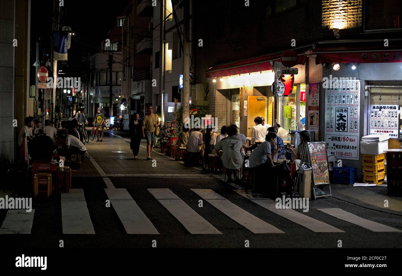 Patrons gather on and around makeshift seats and tables outside of a yakitori restaurant in Tokyo, Japan, on a summer night Stock Photo