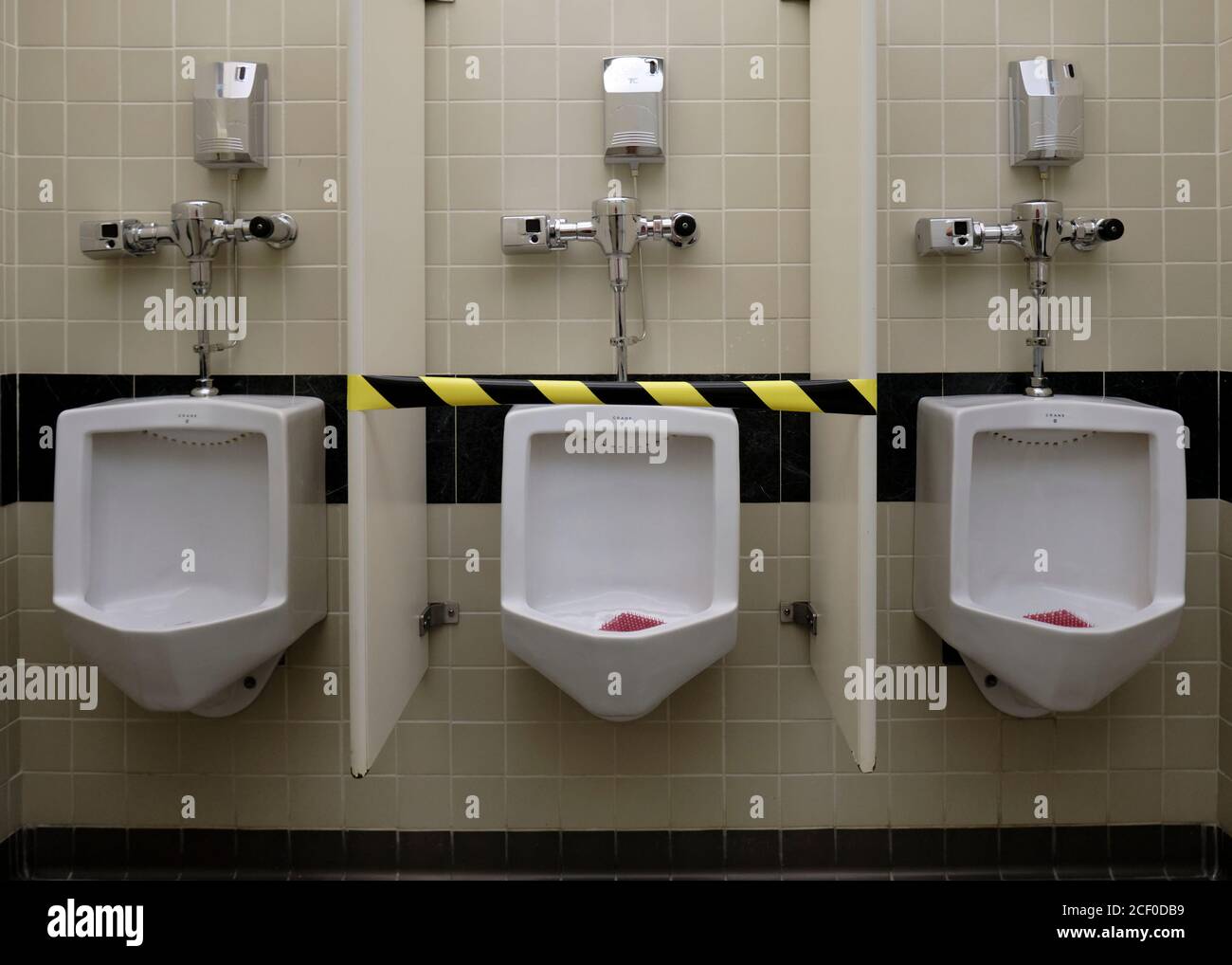 Set of three urinals with the middle one taped up and out of usage