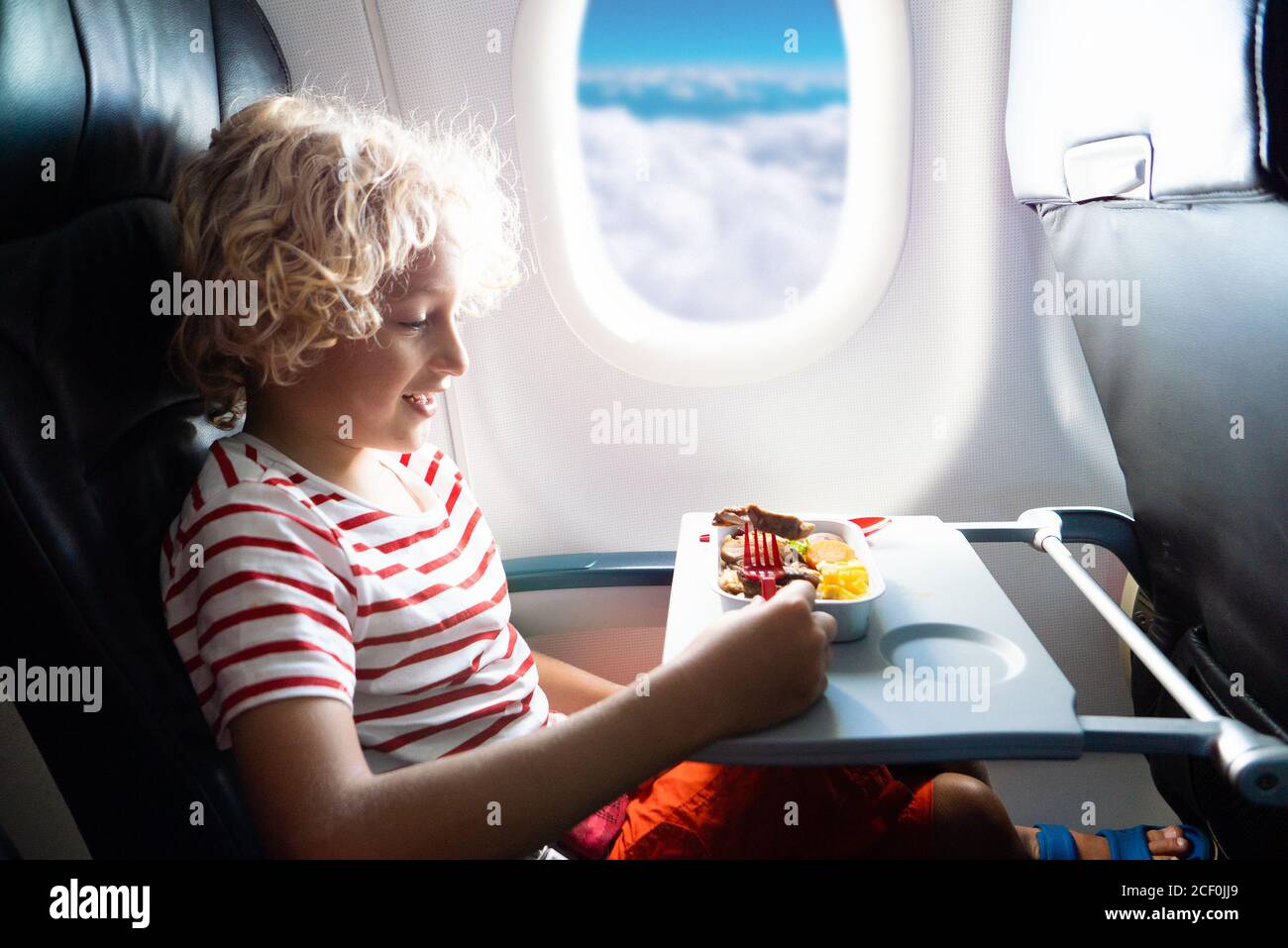 Child in airplane window seat. Kids flight meal. Children fly. Special inflight menu, food and drink for baby and kid. Boy eating healthy lunch in air Stock Photo