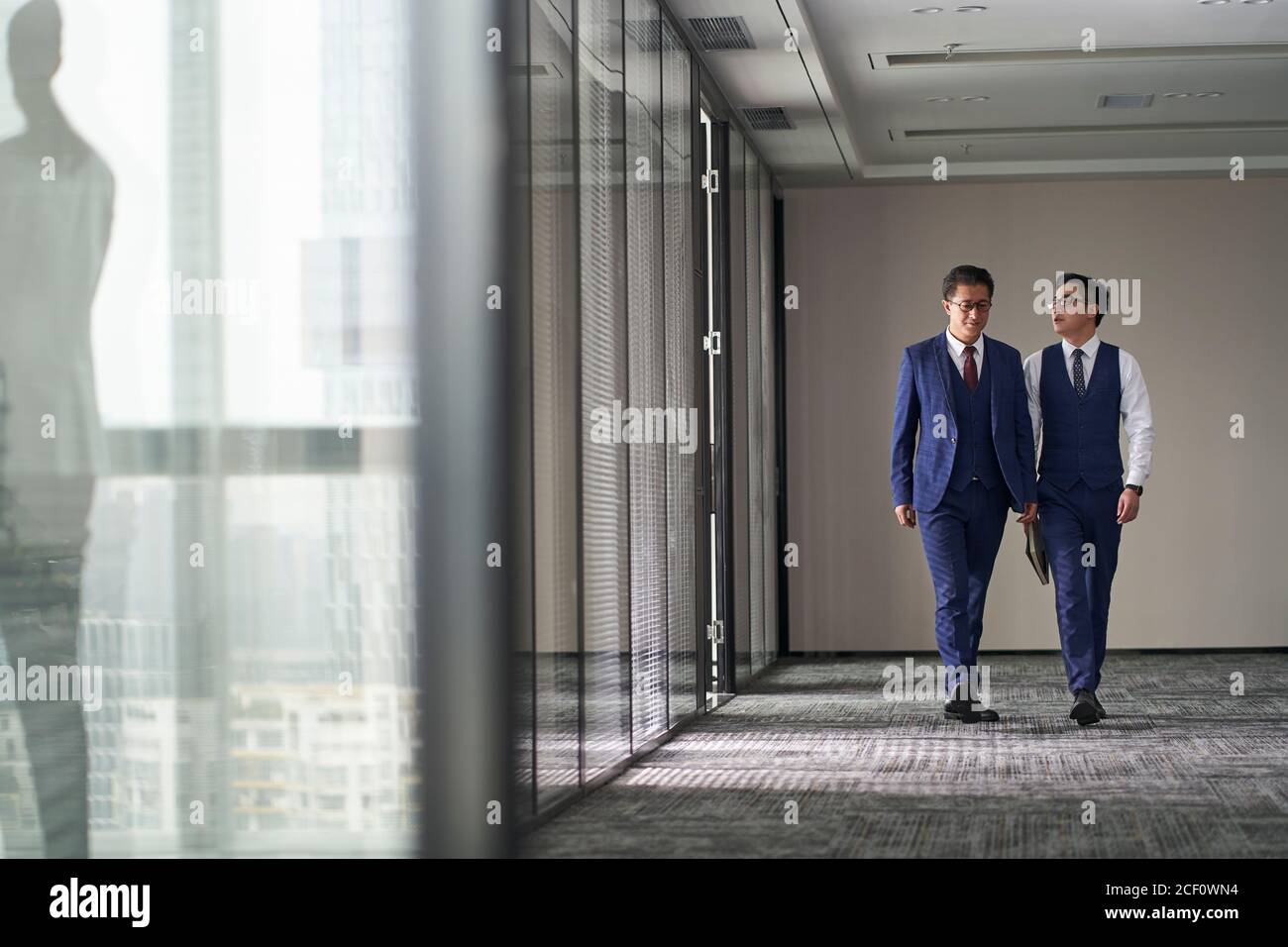 two asian corporate executives discussing business while walking in office Stock Photo