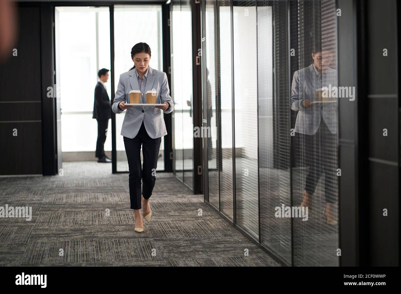 young asian trainee intern carrying a tray of cups of coffee walking in company office Stock Photo