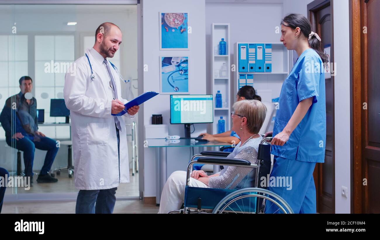 Doctor checking diagnosis of disabled senior woman in wheelchair