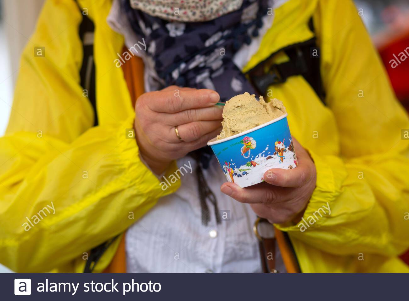 A woman in a yellow rain jacket eats from a tub of ice-cream in Weimar, Germany Stock Photo