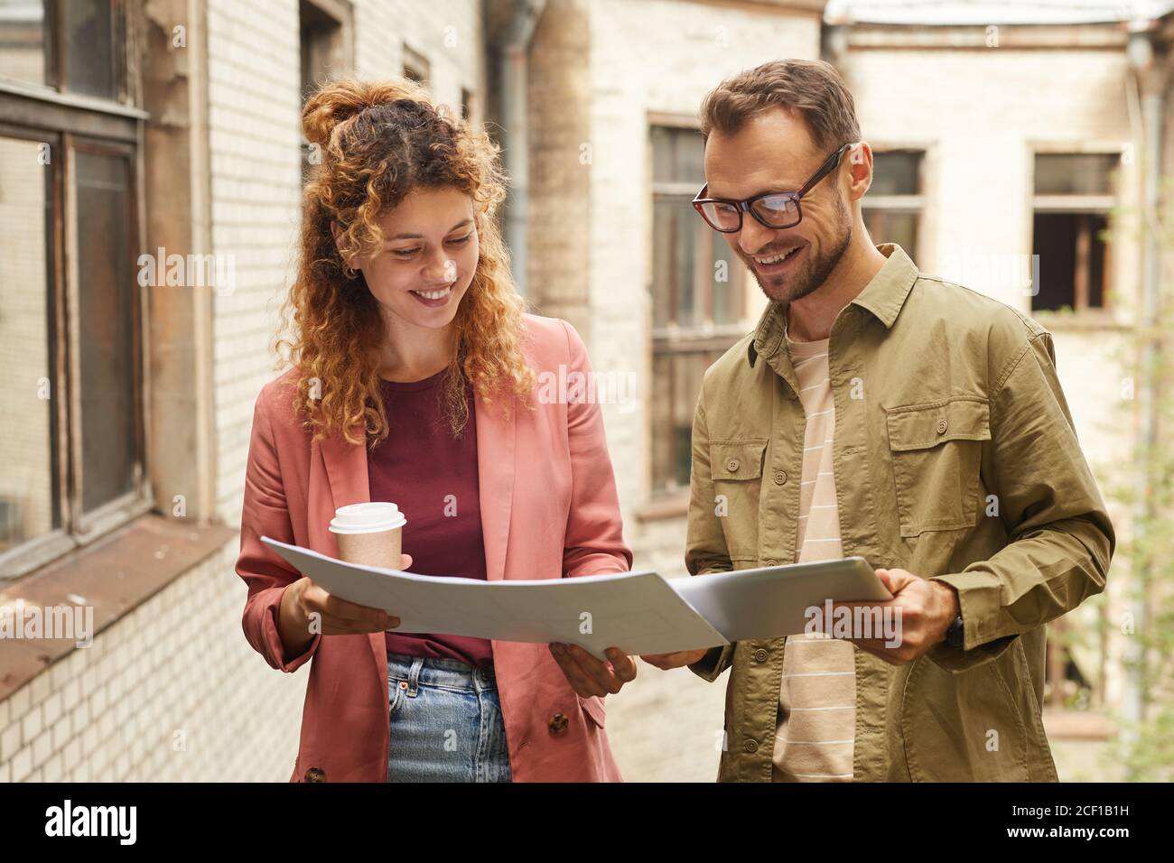 Two successful architects looking at blueprint and using digital tablet while working outdoors Stock Photo