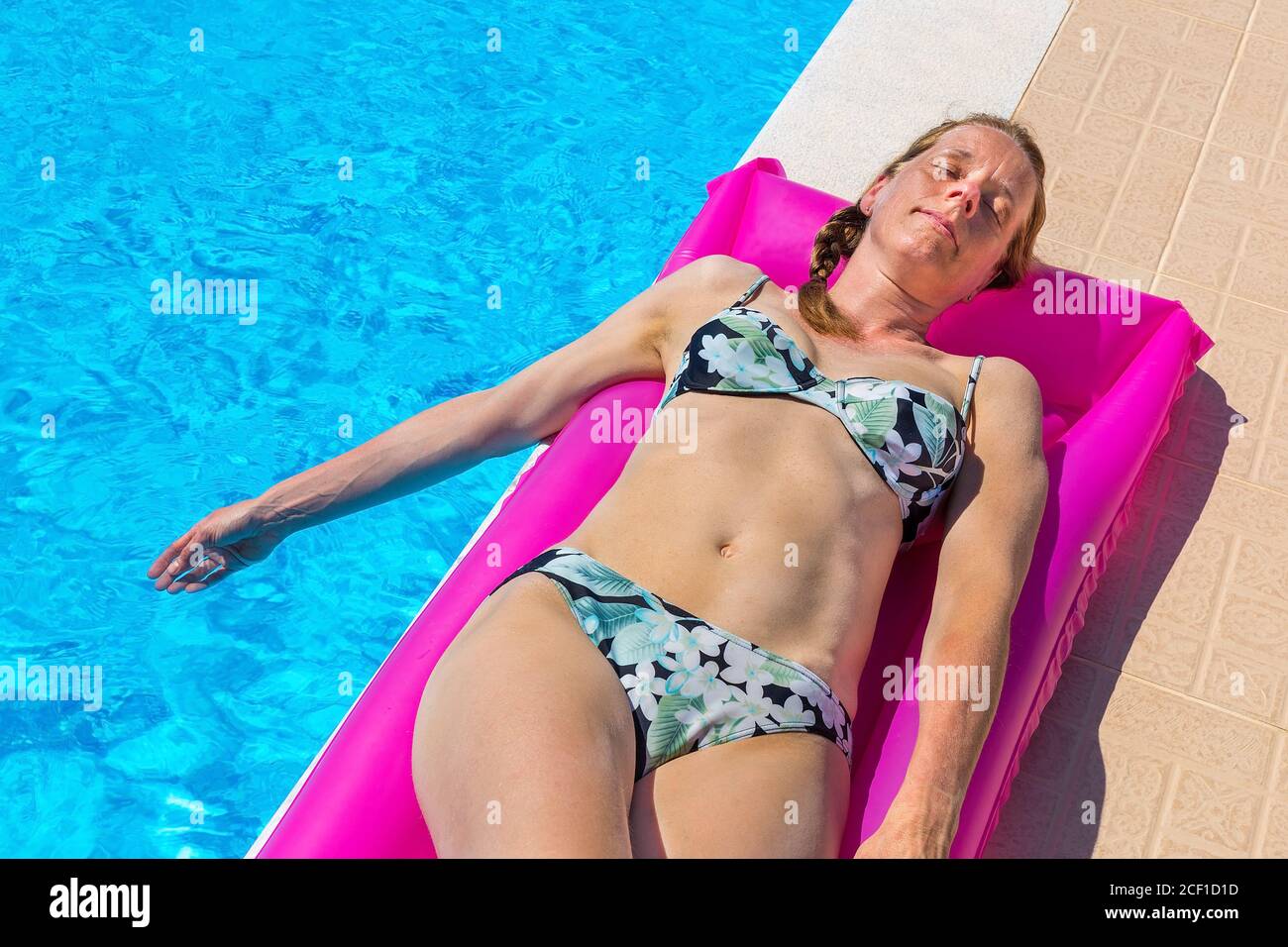 Middle aged european woman lying on air mattress sunbathing at swimming pool Stock Photo