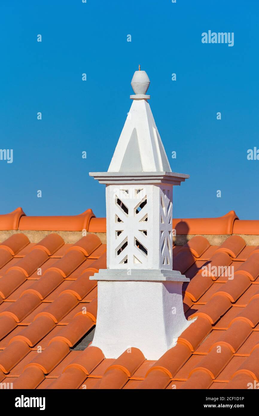 Graceful white chimney with orange roof tiles and blue sky Stock Photo