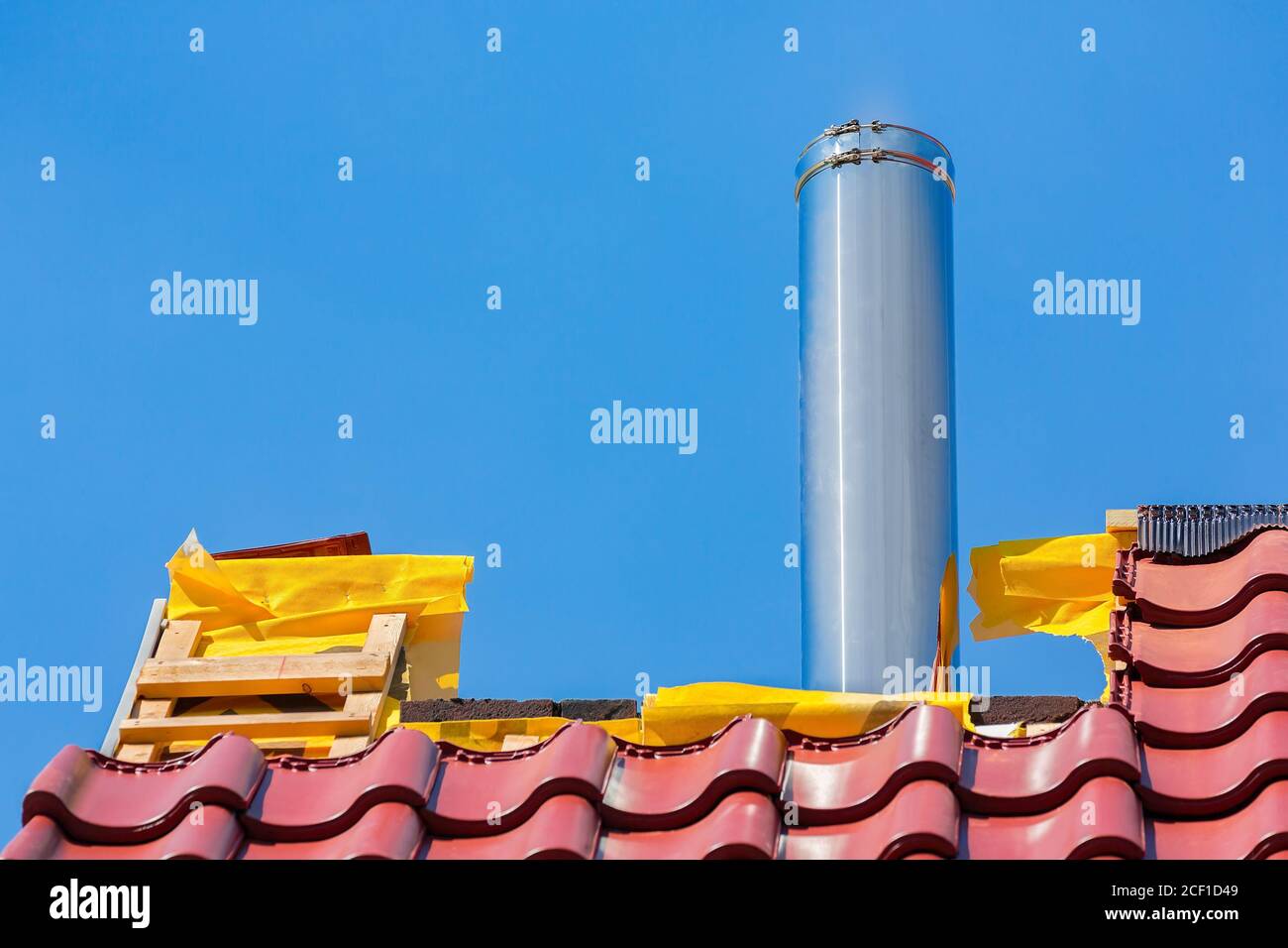 New roof with roof tiles and stainless metal chimney pipe against blue sky Stock Photo
