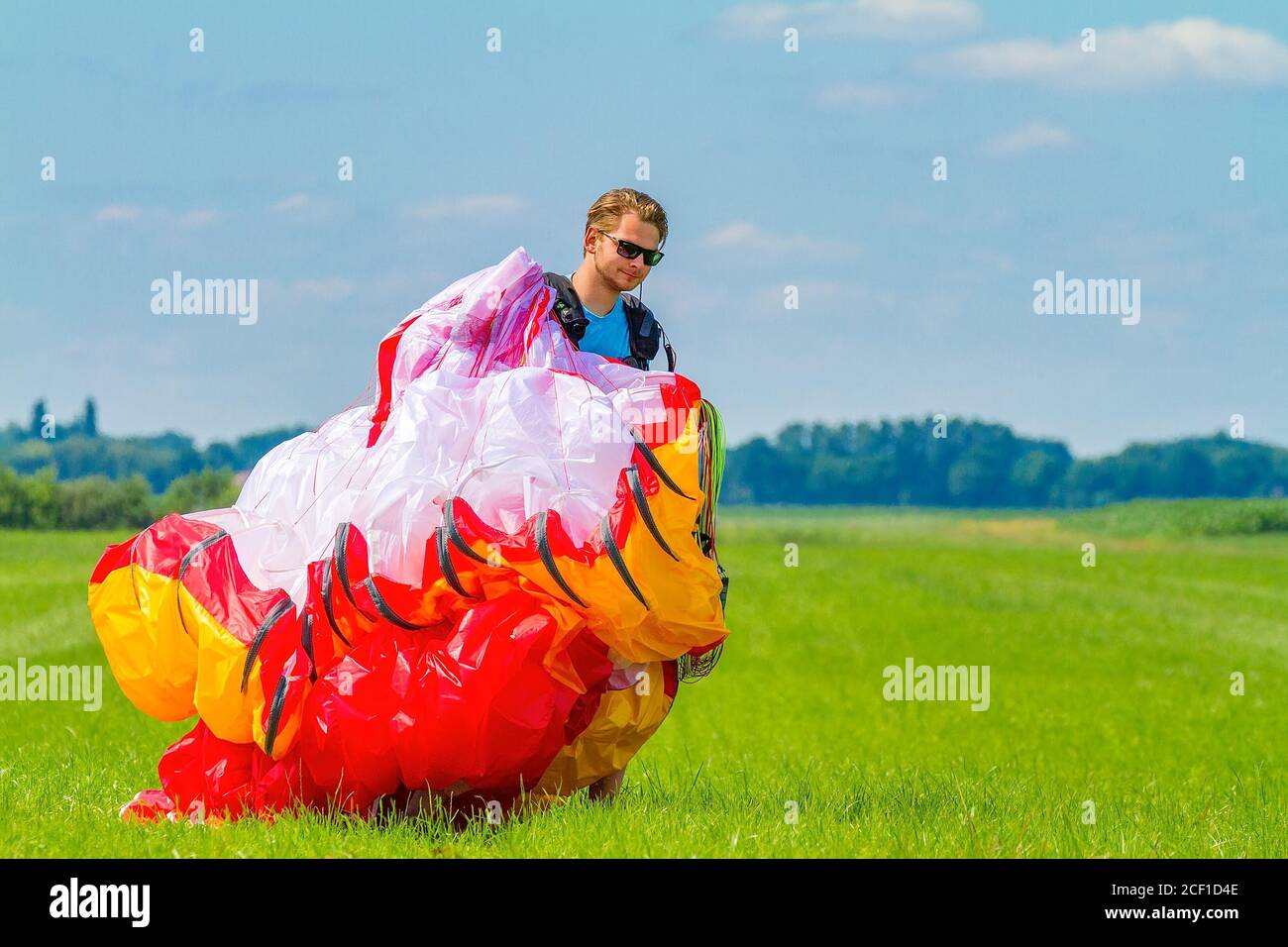 Male dutch paraglider carrying mattress flyer in green meadow Stock Photo