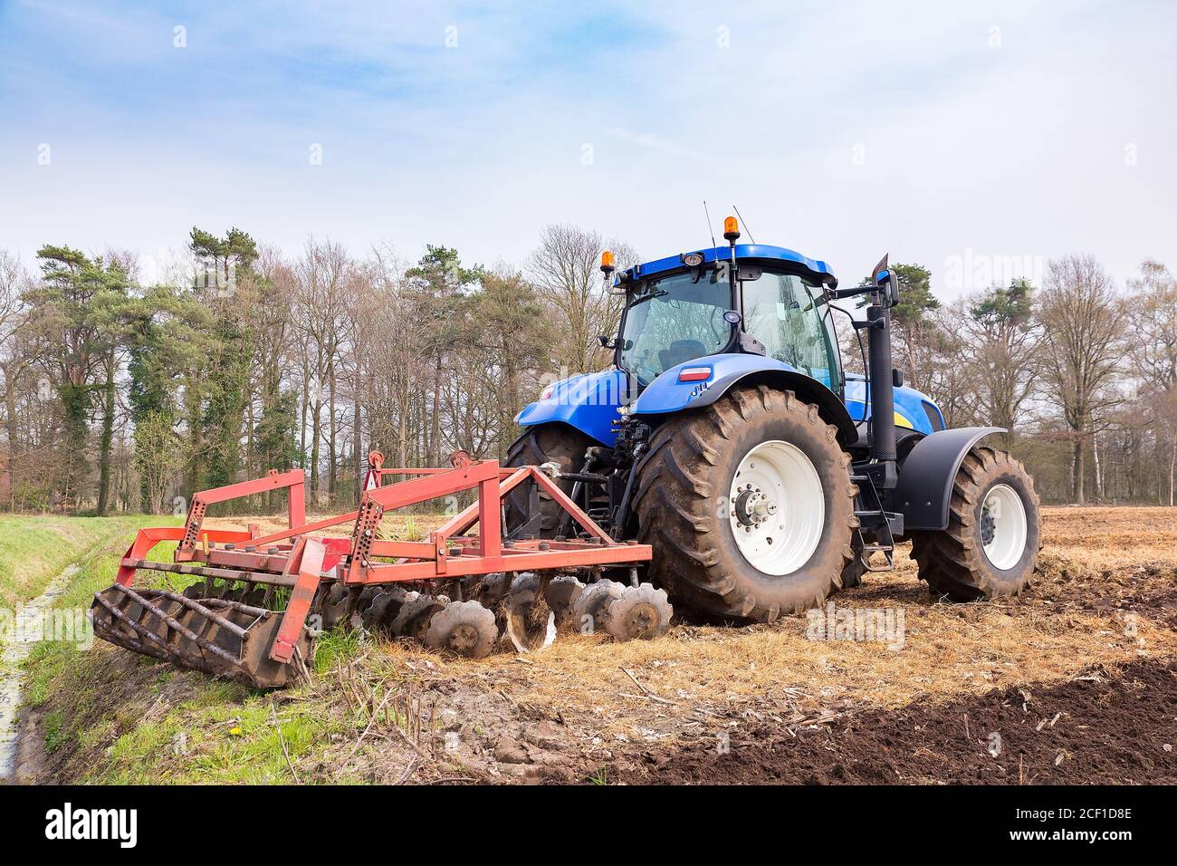 Dutch tractor tills the ground with a harrow in spring season Stock Photo