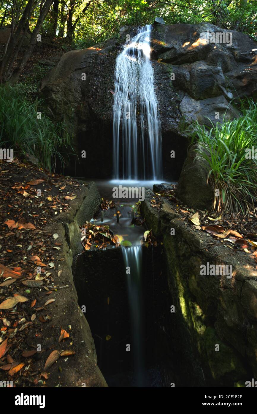 Waterfall in the garden on a long exposure. Blurred water background. Vertical panorama consisting of several frames. Landscape design of the Park. Fo Stock Photo