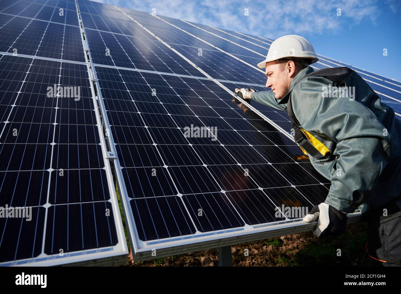 Professional worker, wearing protective suit, helmet and gloves, installing a photovoltaic solar batteries on a sunny day. Concept of alternative energy and power sustainable resources. Stock Photo