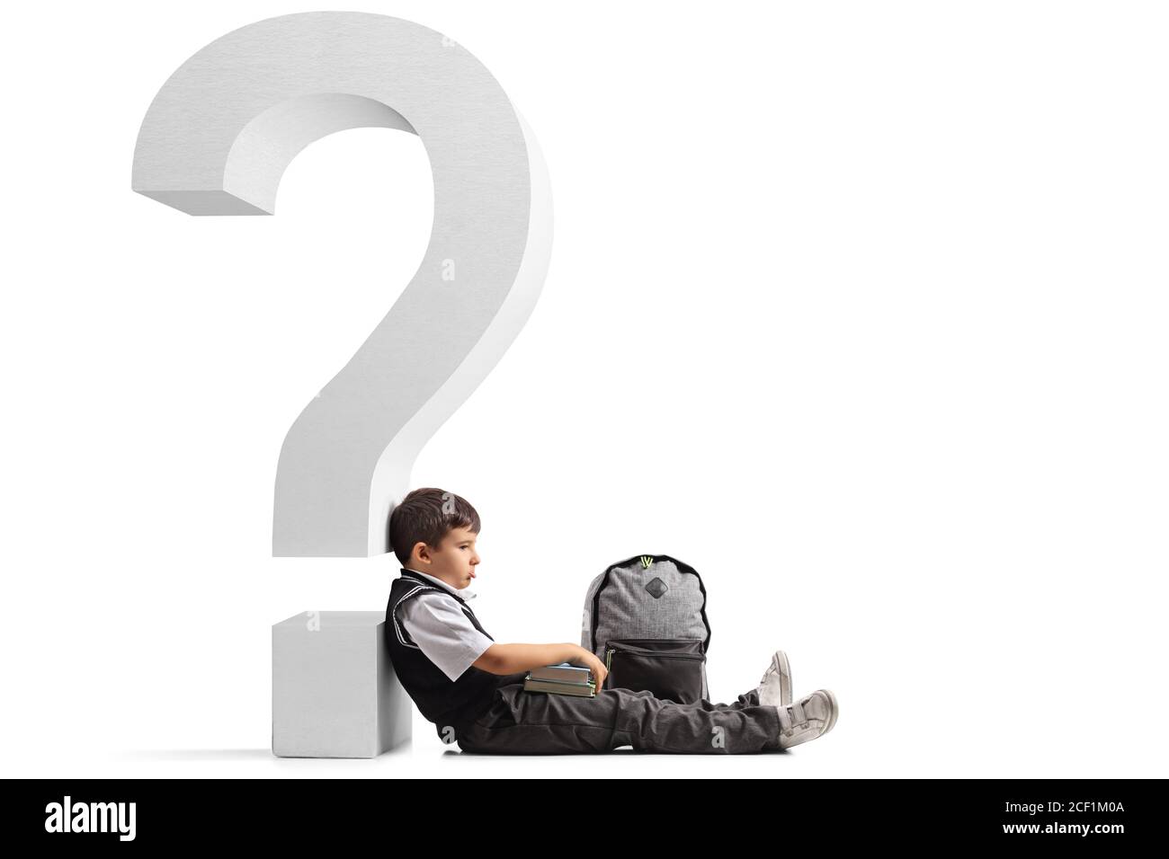 Sad schoolboy with a backpack and books seated on the floor and leaning on a question mark isolated on white background Stock Photo