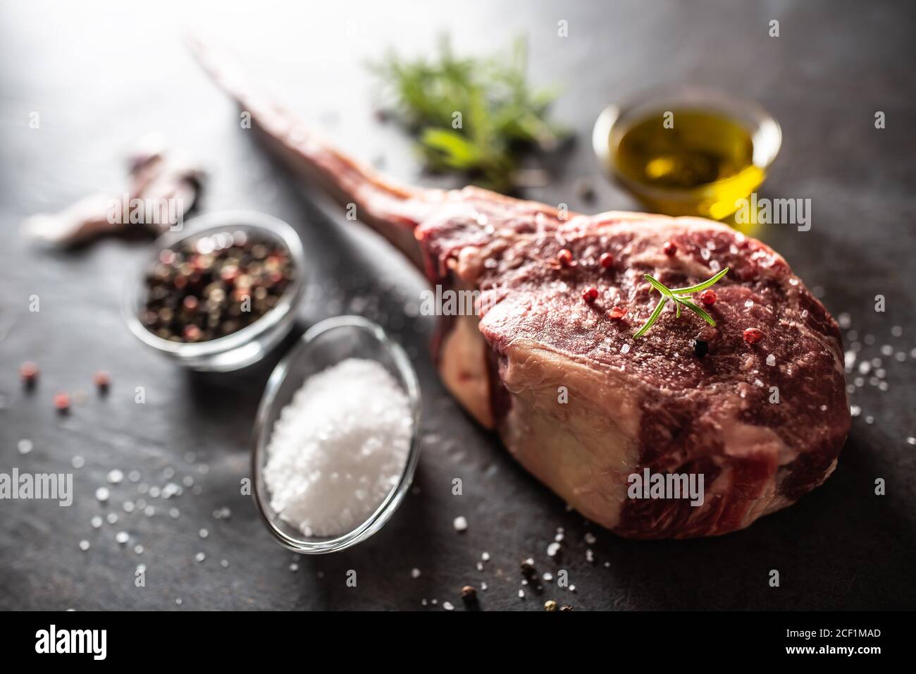 Raw tomahawk steak with salt spices garlic and herbs on a old rustic board Stock Photo