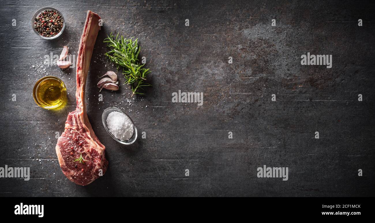 Raw tomahawk steak with salt spices garlic and herbs on a old rustic board - Top of view Stock Photo