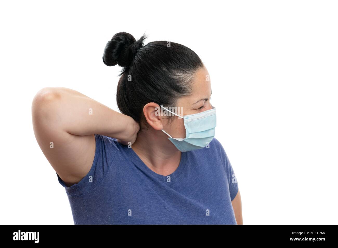 Adult female wearing medical or surgical mask touching back of neck with hand as muscular pain covid19 flu virus infection symptom isolated on white s Stock Photo