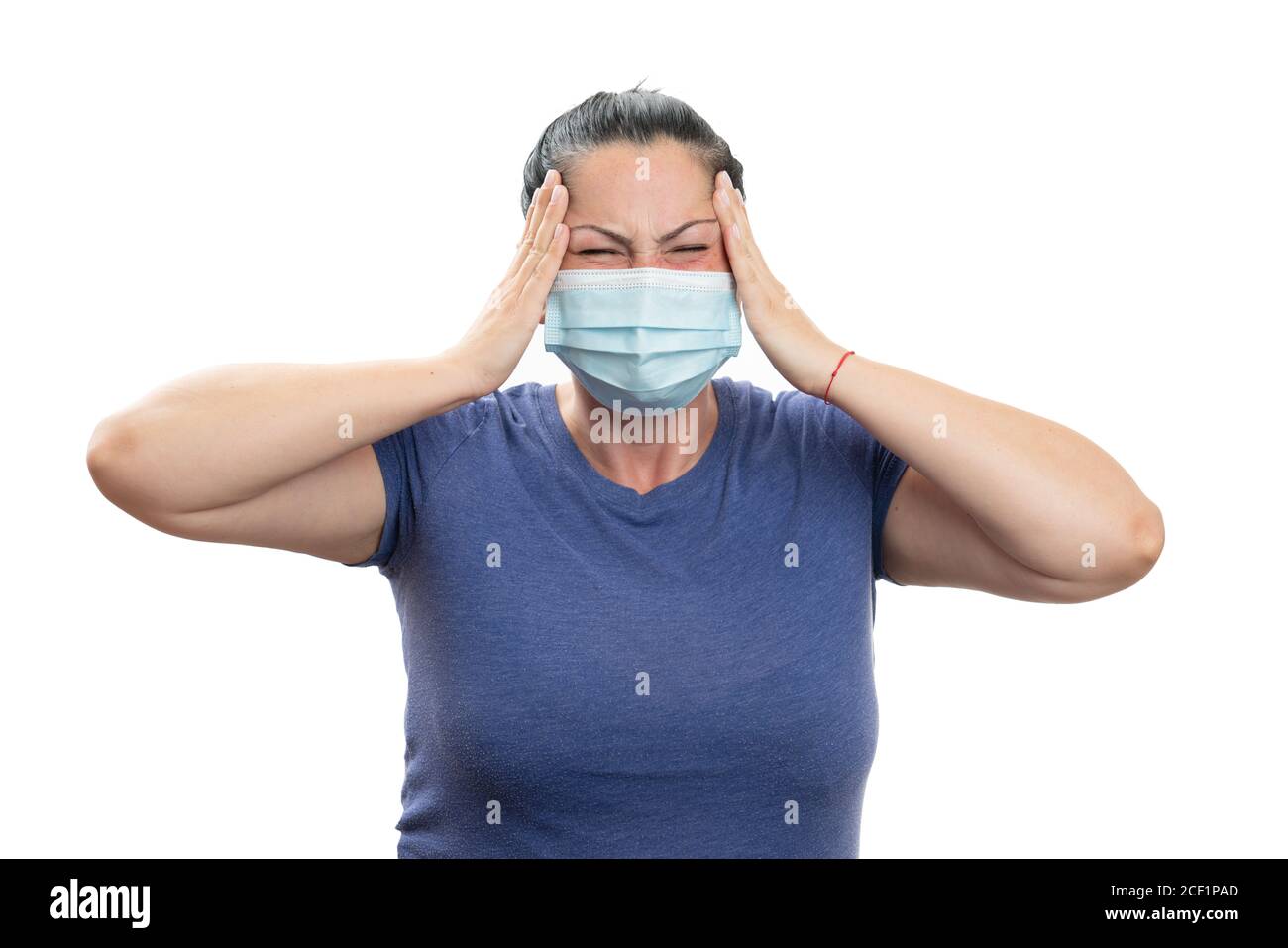 Adult female with headache touching temples as covid19 coronavirus infection flu symptom concept wearing disposable medical or surgical protection mas Stock Photo