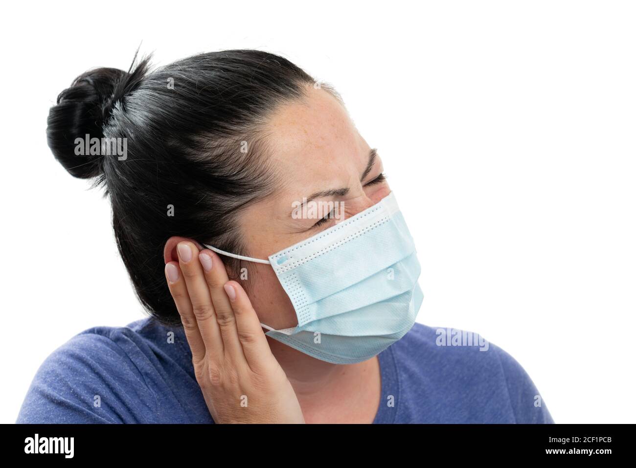 Adult female model touching ear with hand as pain covid19 influenza flu symptom concept wearing surgical disposable mask to protect from contamination Stock Photo