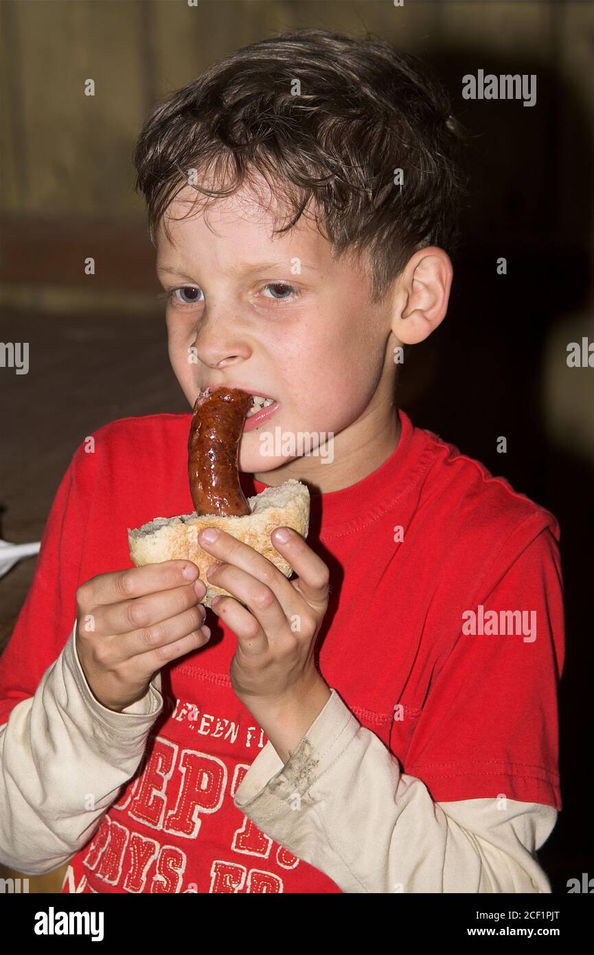 Boy eating sausage with a bun. Junge, der Wurst mit einem Brötchen isst. Niño comiendo salchichas con bollo. Chłopiec gryzie kiełbasę. Stock Photo