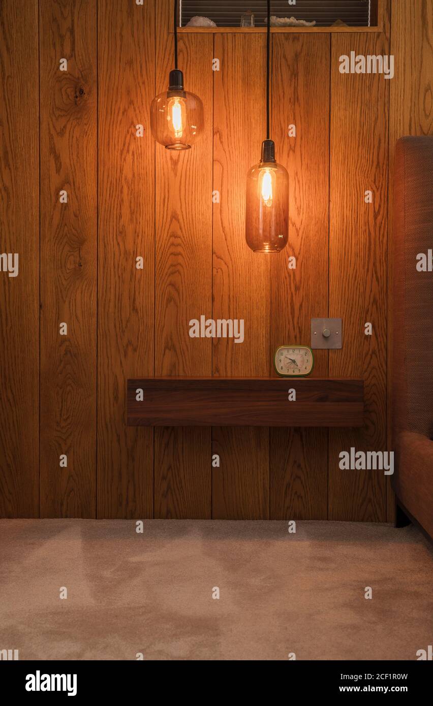 Modern pendant lights hanging over wooden shelf with alarm clock Stock