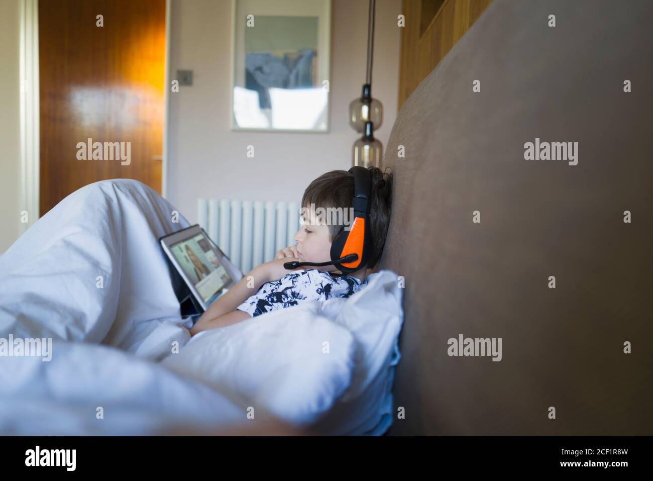 Boy with headphones e-learning with digital tablet in bed Stock Photo