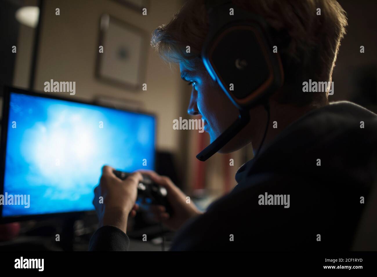 Teenage boy with headset playing video game at computer in dark room