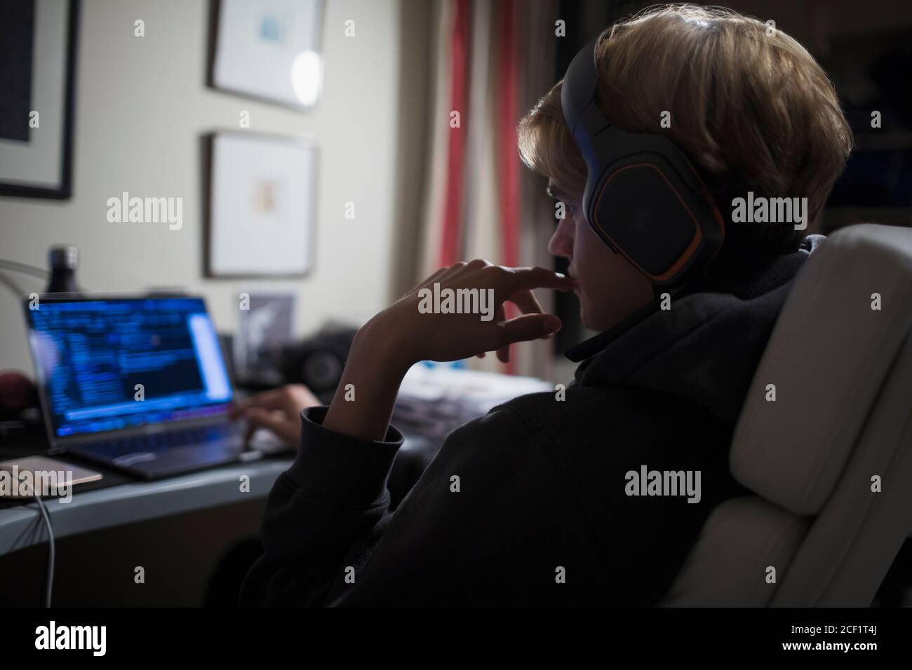 Teenage boy with headphones using computer in dark bedroom Stock Photo ...