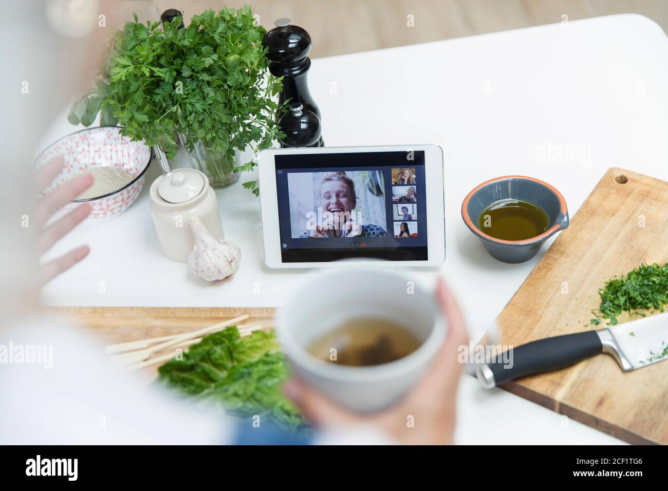 Woman drinking tea and cooking while video chatting with friends Stock Photo