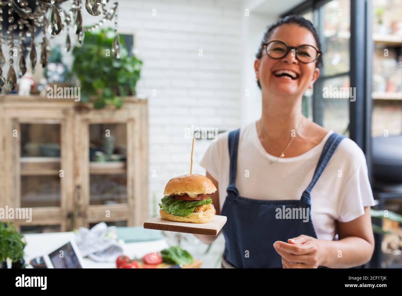 Portrait laughing woman holding cheeseburger on cutting board Stock Photo
