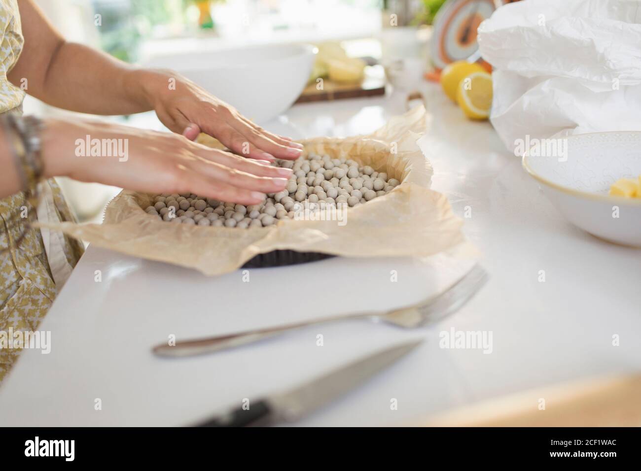 Woman blind baking pie crust with pie weights at kitchen counter Stock