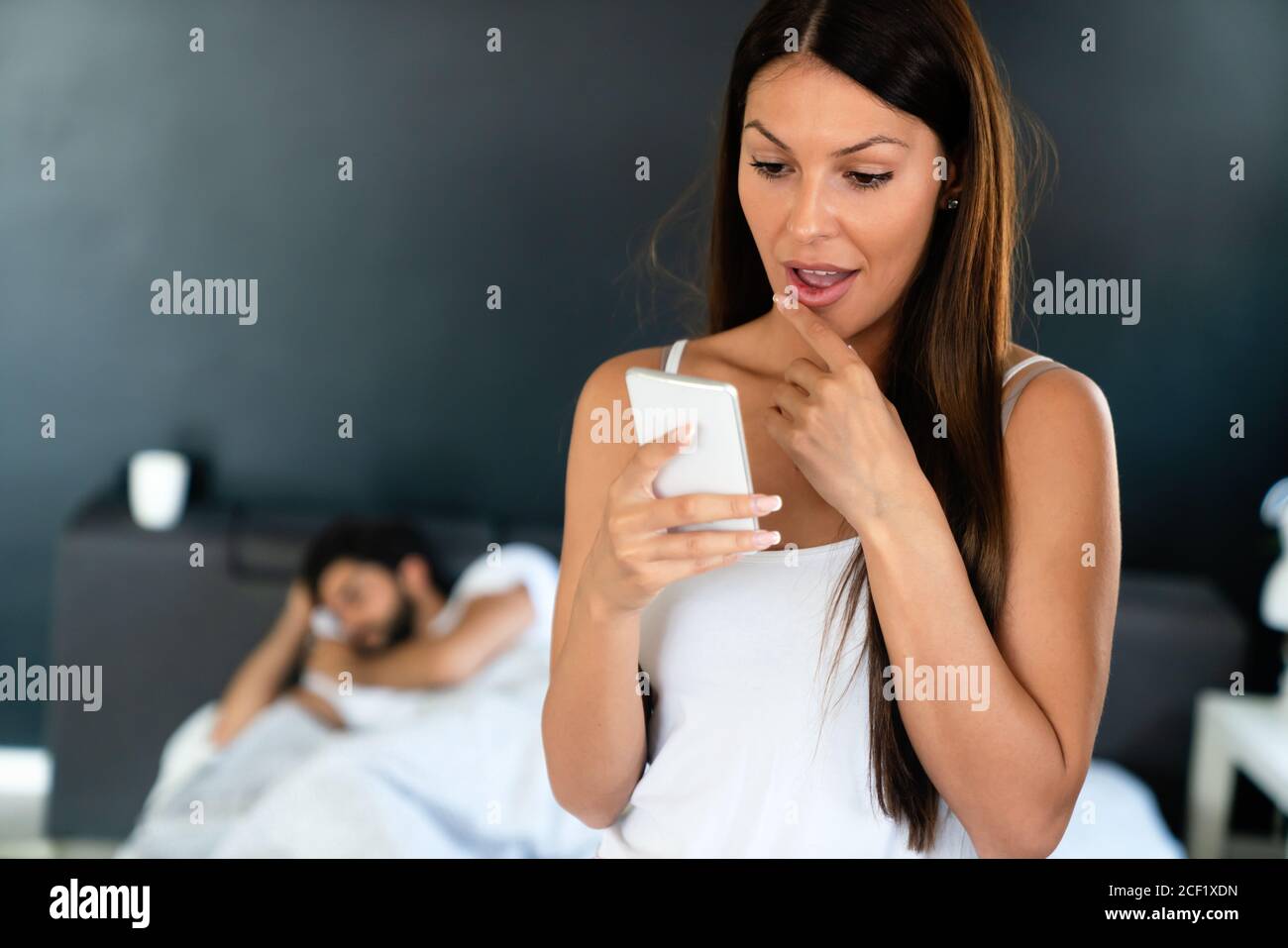 Young woman using cellphone while her husband sleeping on bed Stock Photo