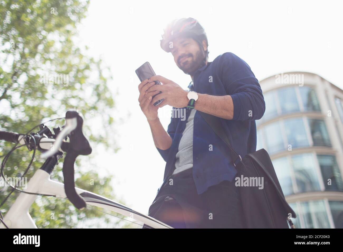 Man using smart phone on bicycle below sunny building Stock Photo